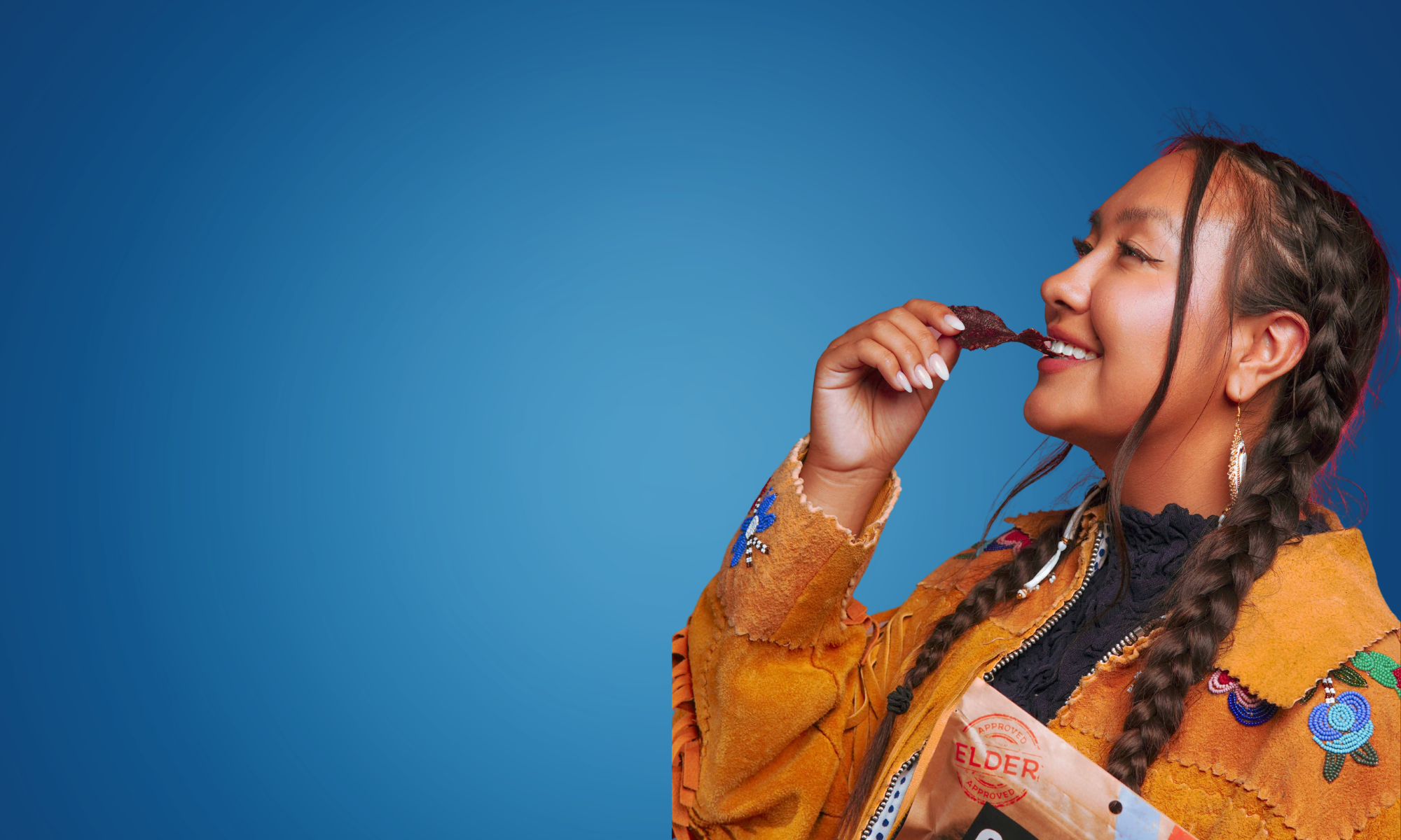 Indigenous woman eating Mitsoh pemmican against a blue background