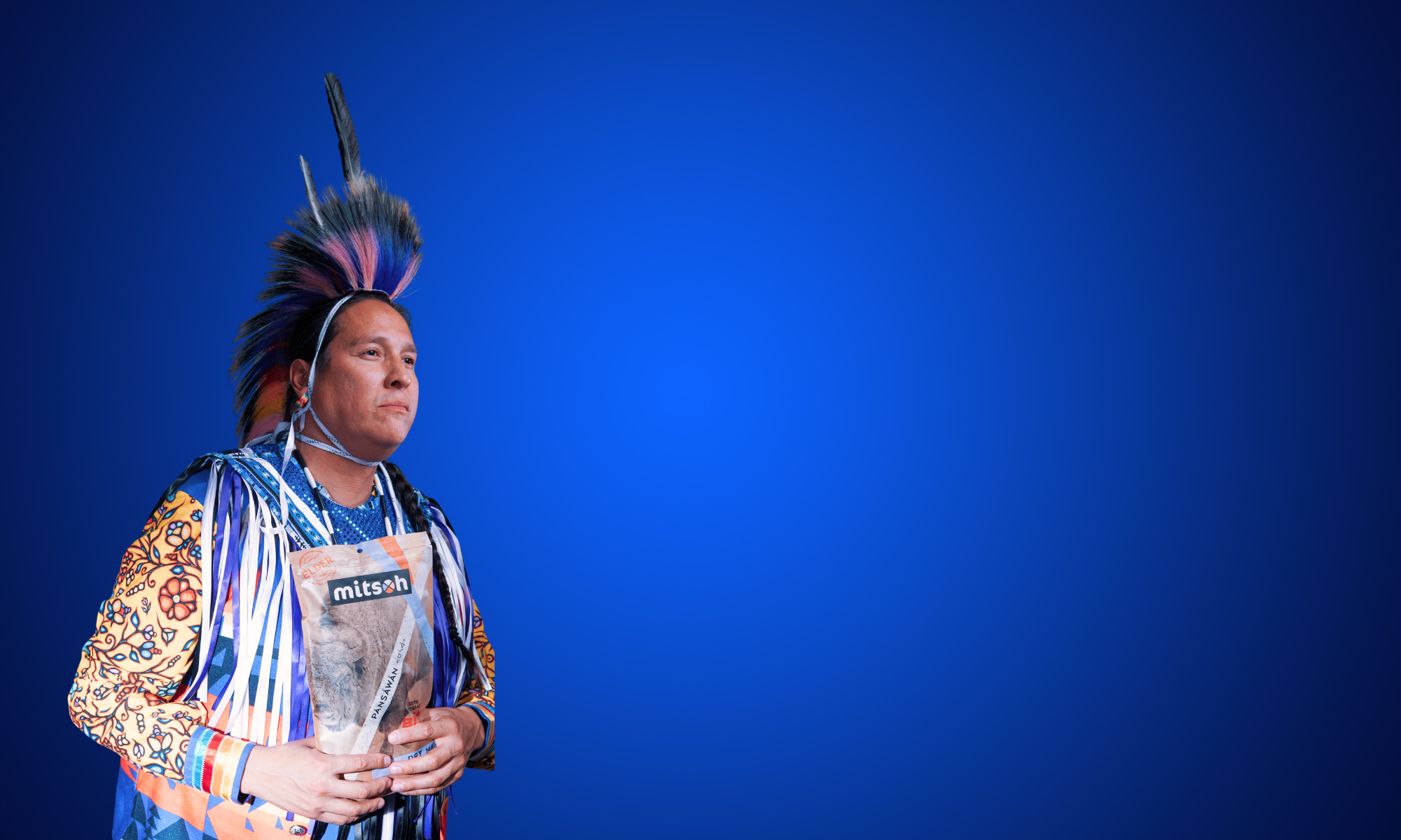 Mitsoh founder Ian Gladue holding a package of Mitsoh dry bison meat against a blue background.