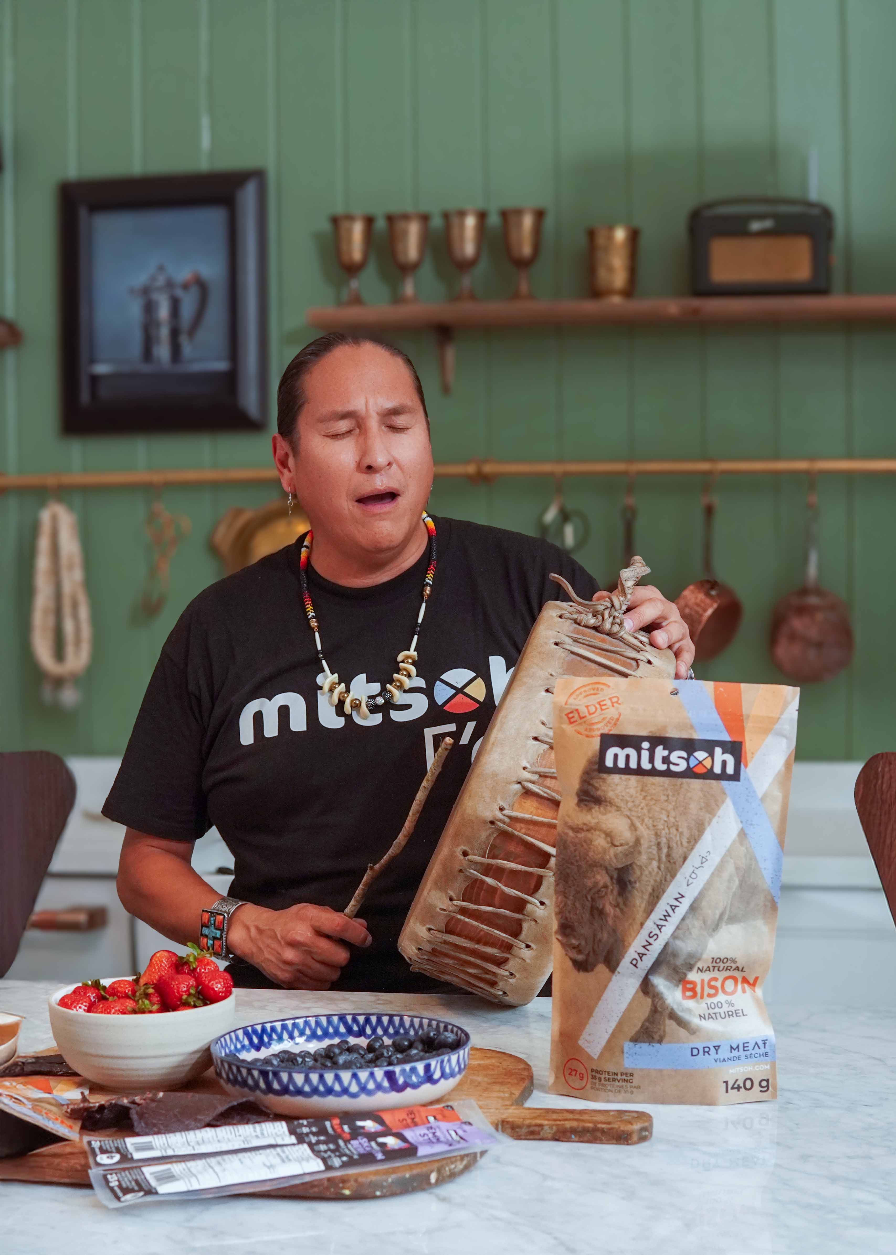 Mitsoh founder Ian Gladue holding a traditional hand drum beside dry bison meat and pemmican