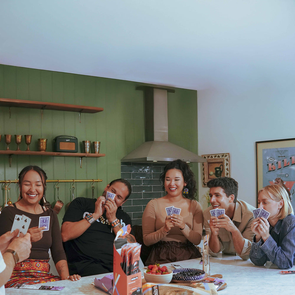 Friends and family gathered around a table playing cards with Mitsoh snacks
